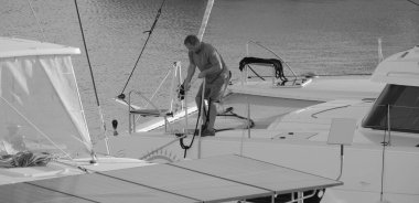 İtalya, Sicilya, Akdeniz, Marina di Ragusa (Ragusa Eyaleti); 4 Ekim 2024, limandaki bir katamaran yelkenli teknesinde adam - EDITORIAL