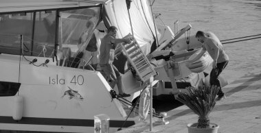 İtalya, Sicilya, Akdeniz, Marina di Ragusa (Ragusa Eyaleti); 4 Ekim 2024, limanda bir katamaran yelkenli teknesinde çift - EDITORIAL