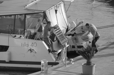 İtalya, Sicilya, Akdeniz, Marina di Ragusa (Ragusa Eyaleti); 4 Ekim 2024, limanda bir katamaran yelkenli teknesinde çift - EDITORIAL