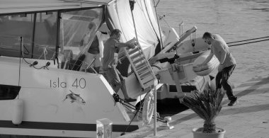 İtalya, Sicilya, Akdeniz, Marina di Ragusa (Ragusa Eyaleti); 4 Ekim 2024, limanda bir katamaran yelkenli teknesinde çift - EDITORIAL