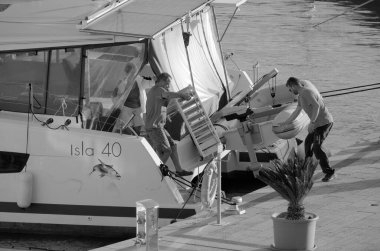 İtalya, Sicilya, Akdeniz, Marina di Ragusa (Ragusa Eyaleti); 4 Ekim 2024, limanda bir katamaran yelkenli teknesinde çift - EDITORIAL