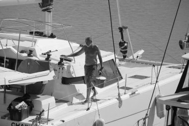 İtalya, Sicilya, Akdeniz, Marina di Ragusa (Ragusa Eyaleti); 6 Ekim 2024, limandaki bir katamaran yelkenli teknesinde adam - EDITORIAL
