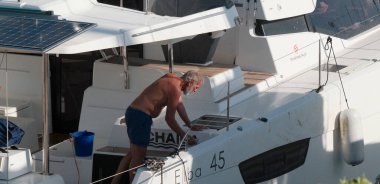 İtalya, Sicilya, Akdeniz, Marina di Ragusa (Ragusa Eyaleti); 6 Ekim 2024, limandaki bir katamaran yelkenli teknesinde adam - EDITORIAL
