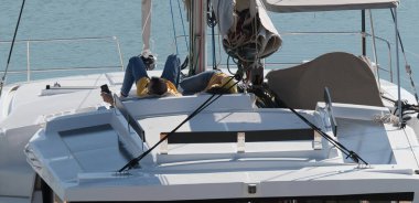 İtalya, Sicilya, Akdeniz, Marina di Ragusa (Ragusa Eyaleti); limandaki bir katamaran yelkenli teknesinde dinlenen çift 