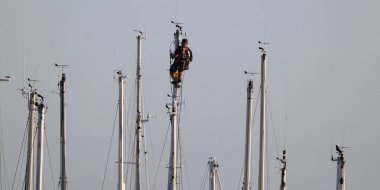 İtalya, Sicilya, Akdeniz, Marina di Ragusa, limanda yelkenli gemi direğinde çalışan adam.