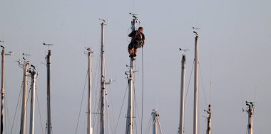 İtalya, Sicilya, Akdeniz, Marina di Ragusa, limanda yelkenli gemi direğinde çalışan adam.