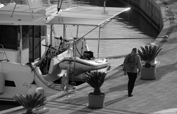 İtalya, Sicilya, Akdeniz, Marina di Ragusa (Ragusa Eyaleti); 9 Aralık 2024, insan ve limanda bir katamaran yelkenli teknesi - EDITORIAL