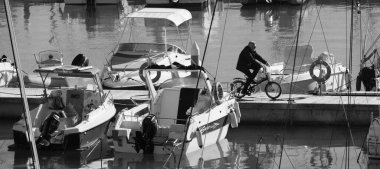 İtalya, Sicilya, Akdeniz, Marina di Ragusa (Ragusa ili); 11 Aralık 2024, limanda bisiklet ve motorlu tekne kullanan adam - EDITORIAL