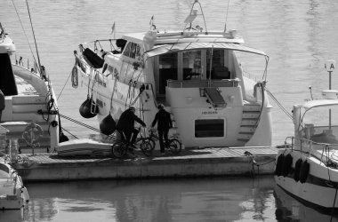 İtalya, Sicilya, Akdeniz, Marina di Ragusa (Ragusa Eyaleti); 11 Aralık 2024, limandaki bisiklet ve lüks yatlarda bir çift - EDITORIAL