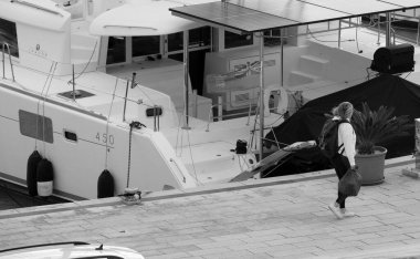 İtalya, Sicilya, Akdeniz, Marina di Ragusa (Ragusa Eyaleti); 20 Aralık 2024, kadın ve limanda bir katamaran yelkenli teknesi - EDITORIAL