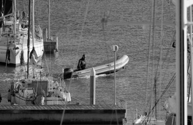 Italy, Sicily, Mediterranean Sea, Marina di Ragusa (Ragusa Province); 5 January 2025, man on a rubber boat and luxury yachts in the port - EDITORIAL clipart