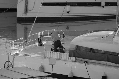 İtalya, Sicilya, Akdeniz, Marina di Ragusa (Ragusa Eyaleti), limandaki katamaran yelkenli teknesinde bir adam. 