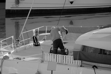 İtalya, Sicilya, Akdeniz, Marina di Ragusa (Ragusa Eyaleti), limandaki katamaran yelkenli teknesinde bir adam. 