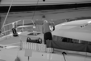 İtalya, Sicilya, Akdeniz, Marina di Ragusa (Ragusa Eyaleti), limandaki katamaran yelkenli teknesinde bir adam. 