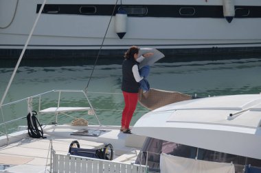 İtalya, Sicilya, Akdeniz, Marina di Ragusa (Ragusa Eyaleti); limandaki katamaran yelkenli teknesinde bir kadın 