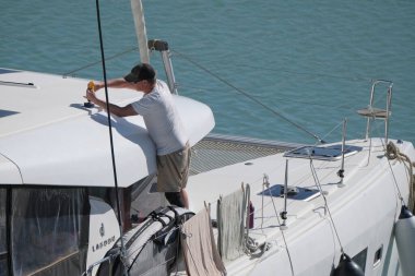 İtalya, Sicilya, Akdeniz, Marina di Ragusa (Ragusa Eyaleti); 17 Şubat 2025, limandaki bir katamaran yelkenli teknesinde adam - EDITORIAL