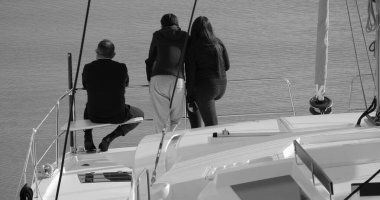 İtalya, Sicilya, Akdeniz, Marina di Ragusa (Ragusa Eyaleti); limandaki bir katamaran yelkenli teknesindeki insanlar 