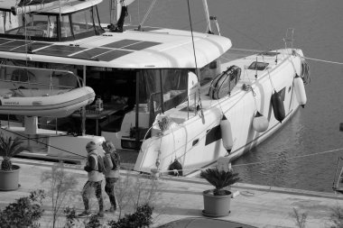 İtalya, Sicilya, Akdeniz, Marina di Ragusa (Ragusa Eyaleti); 4 Mart 2025, limanda insanlar ve bir katamaran yelkenli teknesi - EDITORIAL