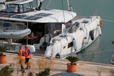 İtalya, Sicilya, Akdeniz, Marina di Ragusa (Ragusa Eyaleti); 4 Mart 2025, limanda insanlar ve bir katamaran yelkenli teknesi - EDITORIAL