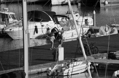 İtalya, Sicilya, Akdeniz, Marina di Ragusa (Ragusa Eyaleti); 5 Mart 2025, limandaki çocuklar elektrikli bisiklet ve lüks yatlar - EDITORIAL