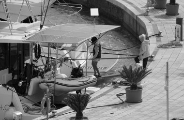 İtalya, Sicilya, Akdeniz, Marina di Ragusa (Ragusa Eyaleti); 16 Nisan 2025, limandaki katamaran yelkenli teknesinde insanlar - EDITORIAL