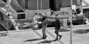İtalya, Sicilya, Akdeniz, Marina di Ragusa (Ragusa Eyaleti); 17 Nisan 2025, limanda insanlar ve bir katamaran yelkenli teknesi - EDITORIAL