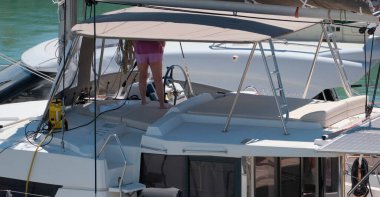 İtalya, Sicilya, Akdeniz, Marina di Ragusa (Ragusa Eyaleti); limanda katamaran yelkenlisini temizleyen kadın 