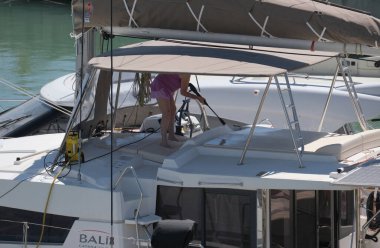 İtalya, Sicilya, Akdeniz, Marina di Ragusa (Ragusa Eyaleti); 1 Mayıs 2025, limanda katamaran yelkenlisini temizleyen kadın - EDITORIAL