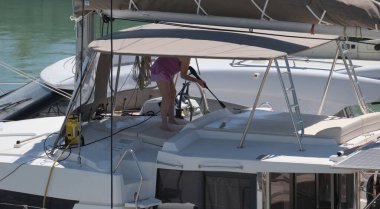 İtalya, Sicilya, Akdeniz, Marina di Ragusa (Ragusa Eyaleti); limanda katamaran yelkenlisini temizleyen kadın 