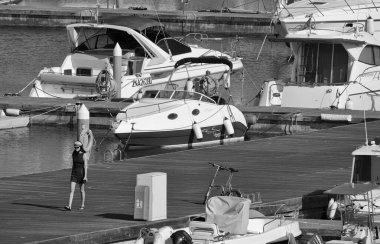 İtalya, Sicilya, Akdeniz, Marina di Ragusa (Ragusa Eyaleti); 7 Mayıs 2025, limandaki kız ve lüks yatlar - EDITORIAL