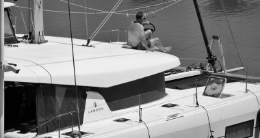 İtalya, Sicilya, Akdeniz, Marina di Ragusa (Ragusa Eyaleti); 3 Haziran 2025, limandaki bir katamaran yelkenli teknesinde adam - EDITORIAL