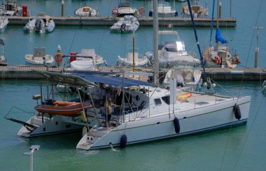 İtalya, Sicilya, Akdeniz, Marina di Ragusa (Ragusa Eyaleti); 6 Haziran 2025, limandaki katamaran yelkenli teknesinde köpekli insanlar - EDITORIAL