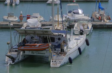 İtalya, Sicilya, Akdeniz, Marina di Ragusa (Ragusa Eyaleti); 6 Haziran 2025, limandaki katamaran yelkenli teknesinde köpekli insanlar - EDITORIAL