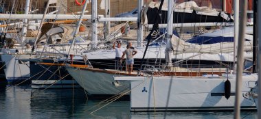 İtalya, Sicilya, Akdeniz, Marina di Ragusa (Ragusa ili); 19 Haziran 2025, limanda bir yelkenli ve lüks yatlarda erkekler - EDITORIAL