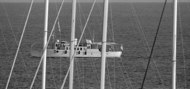 İtalya, Sicilya, Akdeniz, Marina di Ragusa (Ragusa Eyaleti); limanda yelken direkleri ve arka planda lüks bir yat