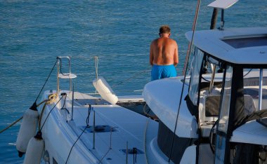 İtalya, Sicilya, Akdeniz, Marina di Ragusa (Ragusa Eyaleti), limandaki katamaran yelkenli teknesinde bir adam. 