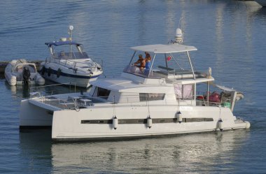 İtalya, Sicilya, Akdeniz, Marina di Ragusa (Ragusa Eyaleti); 13 Temmuz 2025, limandaki katamaran yelkenli teknesinde insanlar - EDITORIAL