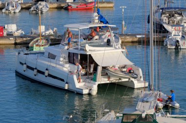 İtalya, Sicilya, Akdeniz, Marina di Ragusa (Ragusa Eyaleti); 13 Temmuz 2025, limandaki katamaran yelkenli teknesinde insanlar - EDITORIAL