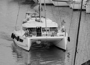 İtalya, Sicilya, Akdeniz, Marina di Ragusa (Ragusa Eyaleti); 13 Temmuz 2025, limandaki katamaran yelkenli teknesinde insanlar - EDITORIAL