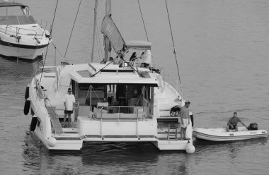 İtalya, Sicilya, Akdeniz, Marina di Ragusa (Ragusa Eyaleti); 13 Temmuz 2025, limandaki katamaran yelkenli teknesinde insanlar - EDITORIAL