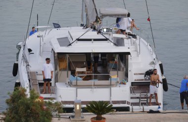 İtalya, Sicilya, Akdeniz, Marina di Ragusa (Ragusa Eyaleti); 13 Temmuz 2025, limandaki katamaran yelkenli teknesinde insanlar - EDITORIAL