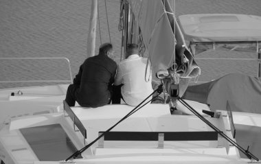 İtalya, Sicilya, Akdeniz, Marina di Ragusa (Ragusa Eyaleti); limandaki katamaran yelkenli teknesinde erkekler 