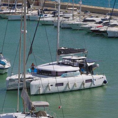 İtalya, Sicilya, Akdeniz, Marina di Ragusa (Ragusa Eyaleti); 22 Temmuz 2025, limandaki katamaran yelkenli teknesinde insanlar - EDITORIAL