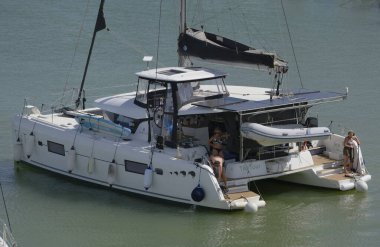 İtalya, Sicilya, Akdeniz, Marina di Ragusa (Ragusa Eyaleti); 22 Temmuz 2025, limandaki katamaran yelkenli teknesinde insanlar - EDITORIAL