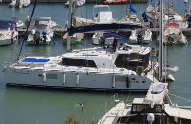 İtalya, Sicilya, Akdeniz, Marina di Ragusa (Ragusa Eyaleti); 25 Temmuz 2025, limandaki katamaran yelkenli teknesinde insanlar - EDITORIAL