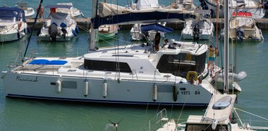 İtalya, Sicilya, Akdeniz, Marina di Ragusa (Ragusa Eyaleti); 25 Temmuz 2025, limandaki katamaran yelkenli teknesinde insanlar - EDITORIAL