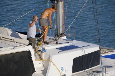 İtalya, Sicilya, Akdeniz, Marina di Ragusa (Ragusa Eyaleti); 2 Ağustos 2025, limanda katamaran yelkenli teknesini temizleyen çift - EDITORIAL