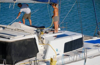 İtalya, Sicilya, Akdeniz, Marina di Ragusa (Ragusa Eyaleti); 2 Ağustos 2025, limanda katamaran yelkenli teknesini temizleyen çift - EDITORIAL