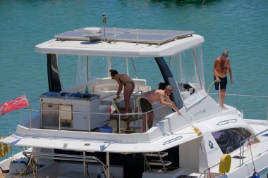 İtalya, Sicilya, Akdeniz, Marina di Ragusa (Ragusa Eyaleti); 4 Ağustos 2025, limanda katamaran yelkenli teknesi temizleyen insanlar - EDITORIAL