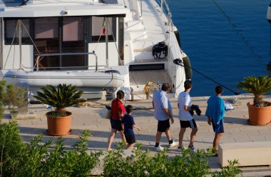 İtalya, Sicilya, Akdeniz, Marina di Ragusa (Ragusa Eyaleti); limanda insanlar ve bir katamaran yelkenlisi 